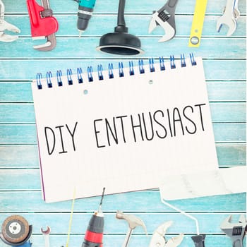 The word diy enthusiast against tools and notepad on wooden background