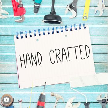 The word hand crafted against tools and notepad on wooden background