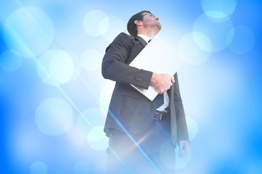 Businessman looking up holding laptop against blue abstract light spot design