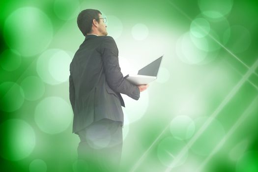 Businessman looking up holding laptop against green abstract light spot design