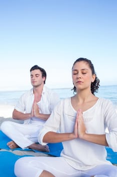 Happy couple doing yoga beside the water at the beach