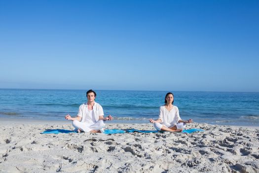 Happy couple doing yoga beside the water at the beach