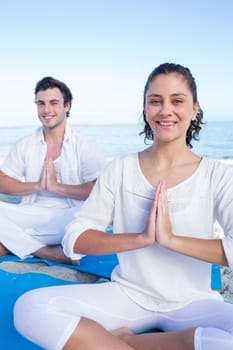 Happy couple doing yoga beside the water at the beach