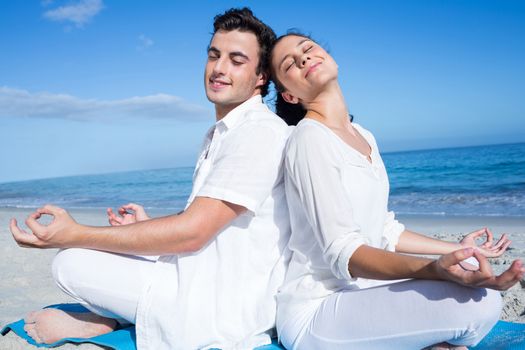 Happy couple doing yoga beside the water at the beach