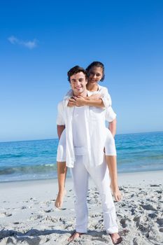 Handsome man giving piggy back to his girlfriend at the beach