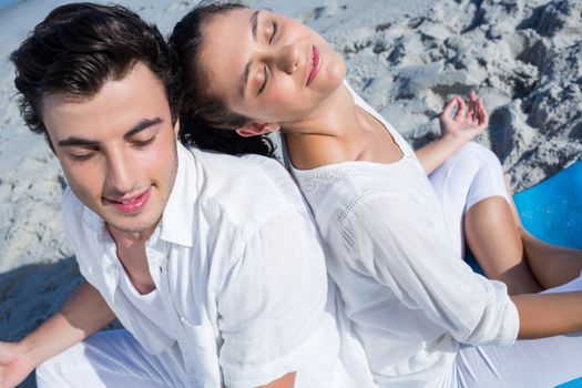 Happy couple doing yoga beside the water at the beach