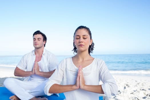 Happy couple doing yoga beside the water at the beach