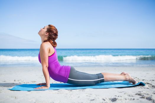 Brunette doing yoga on exercise mat at the beach