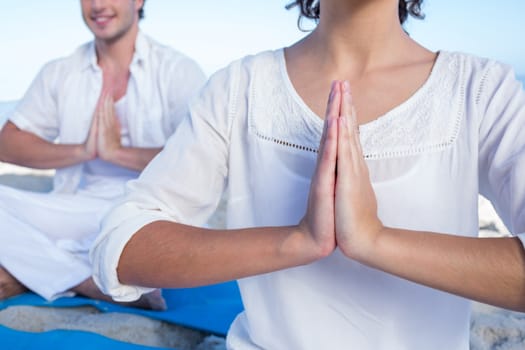 Happy couple doing yoga beside the water at the beach