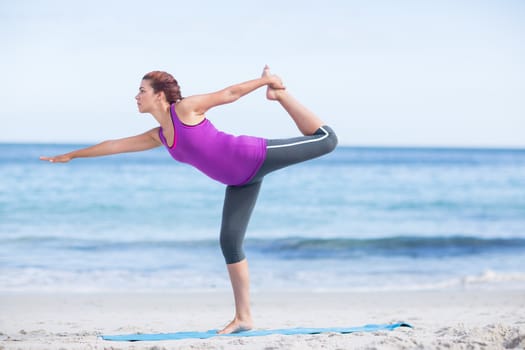 Brunette doing yoga on exercise mat at the beach