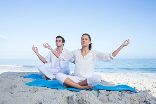 Happy couple doing yoga beside the water at the beach