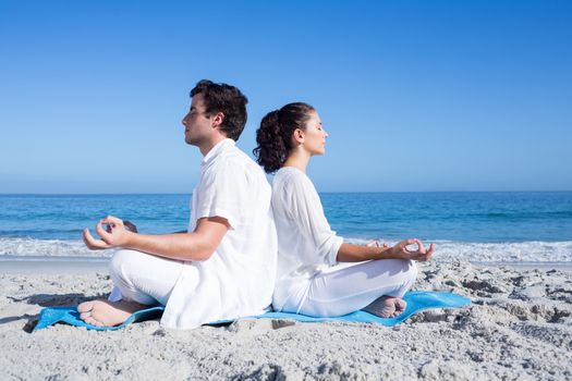 Happy couple doing yoga beside the water at the beach