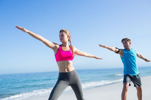 Happy couple doing yoga beside the water at the beach