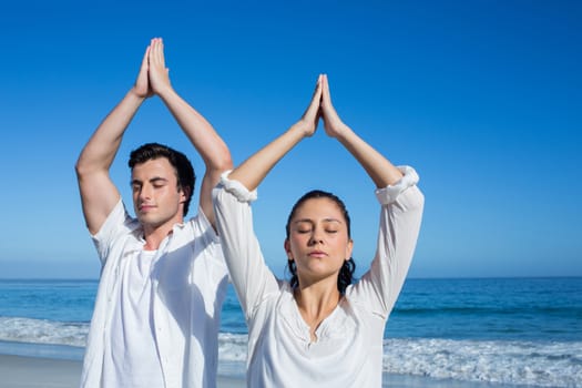 Happy couple doing yoga beside the water at the beach