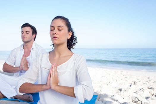 Happy couple doing yoga beside the water at the beach