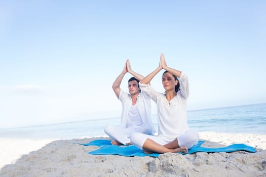Happy couple doing yoga beside the water at the beach