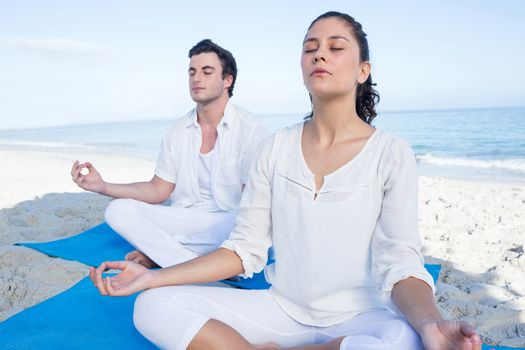 Happy couple doing yoga beside the water at the beach