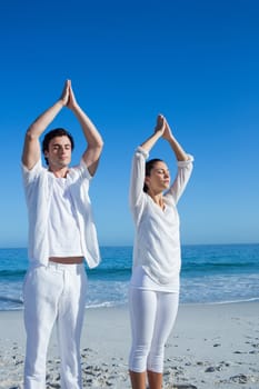 Happy couple doing yoga beside the water at the beach