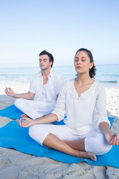 Happy couple doing yoga beside the water at the beach