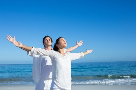 Happy couple doing yoga beside the water at the beach