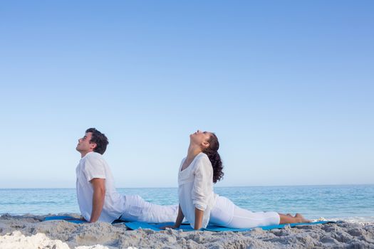 Happy couple doing yoga beside the water at the beach