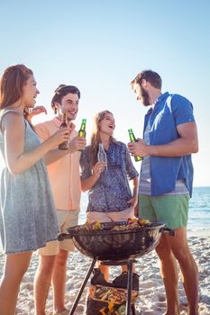 Happy friends doing barbecue and drinking beer at the beach