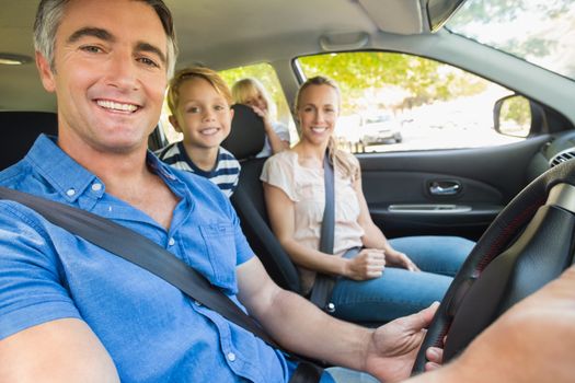 Happy family smiling at the camera in the car on a sunny day