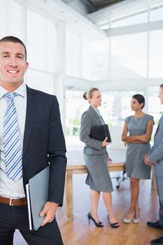Businessman smiling at camera with colleagues behind him in the office