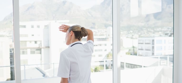 Wear view of confident female doctor looking through windows in hospital