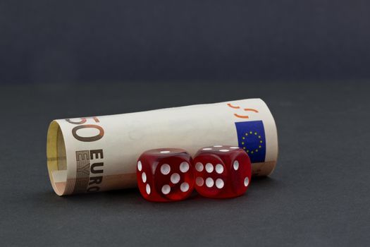 Pair of red dice in front of euro money placed on simple, dark background depicts financial policies and business environments with chance and risk. 