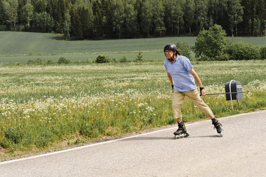 Senior man vigorously exercising. He is Nordic inline skating on a country road by the fields. THere's a post box at the side of the road