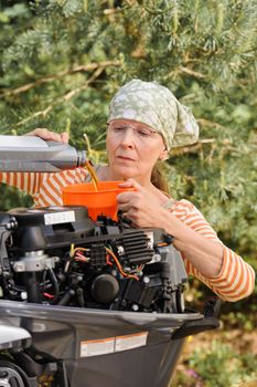 Senior woman pours oil into an outboard engine through a funnel. Breaking down the  stereotypes of women - gender and age