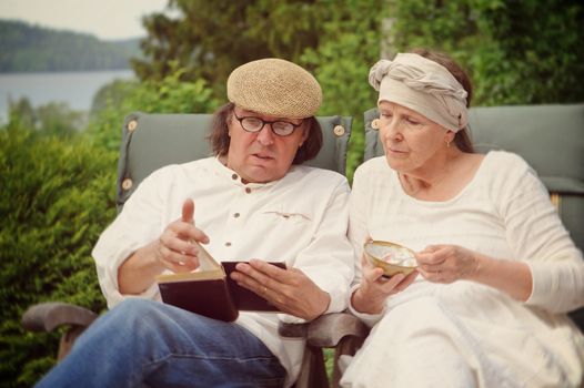 senior couple look at a book together. She's eating yoghurt from a bowl. Digital filters have been used to create a retro look