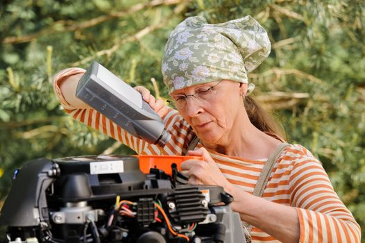 Senior woman pours oil into an outboard engine through a funnel. Breaking down the  stereotypes of women - gender and age