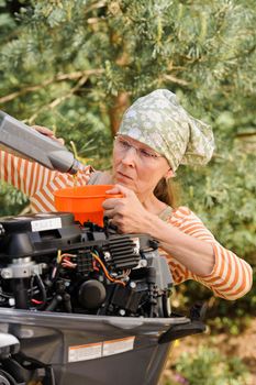 Senior woman pours oil into an outboard engine through a funnel. Breaking down the  stereotypes of women - gender and age