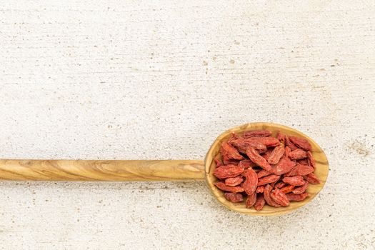 dried goji berries on a wooden spoon against a grunge barn wood with a copy space