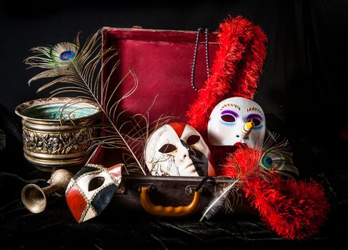 Bright, decorated porcelain mask for decorations and celebrations, and red suitcase peacock, and boa feathers