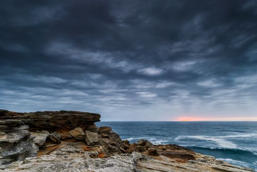 Sunrise seascape with orange rocks and ocean pools and sea shells with cloudy stormy sky and distant cliffs