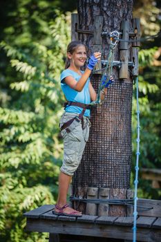 Happy school girl enjoying activity in a climbing adventure park on a summer day