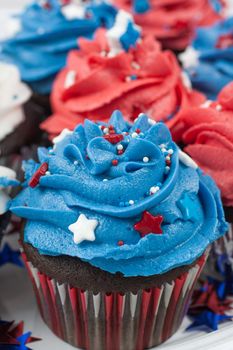 Chocolate cupcakes decorated in red, white, and blue and surrounded by stars and flags in celebration of  Independence Day.