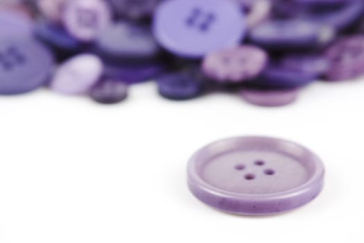 Close up of various purple button scattered on a white surface.