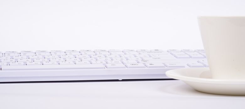 Computer keyboard and cup on isolated white background, side view