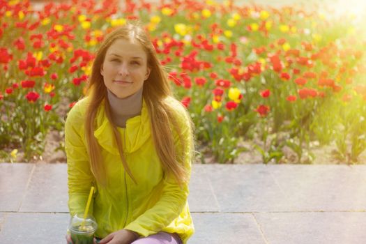 blond girl sitting next to a flower bed