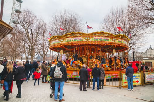 LONDON - APRIL 4: Carousel at the Thames riverbank crowded with tourists on April 4, 2015 in London, UK. London is a popular centre for tourism, one of its prime industries, employing the equivalent of 350,000 full-time workers.