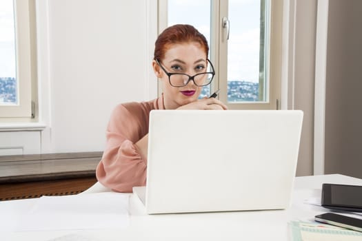 Sitting Young Businesswoman Writing on a Paper While Looking at her Laptop Computer Seriously.