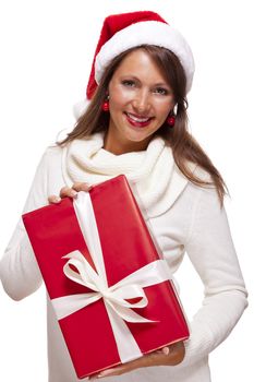 Pretty woman in a festive red Santa hat with a large matching red Christmas gift tied with a ribbon and bow holding it in front of her with a happy smile showing it to the camera, on white