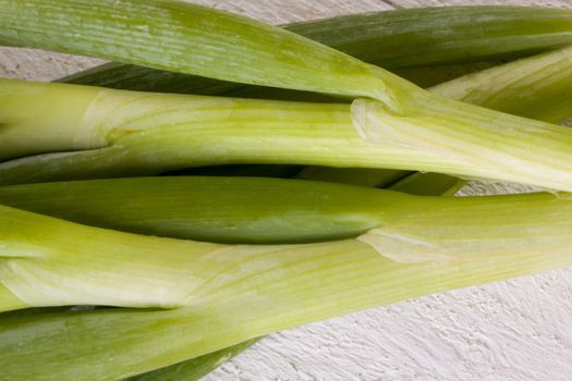 Overhead view of a bunch of fresh leafy leeks or scallions lying on white painted wooden boards