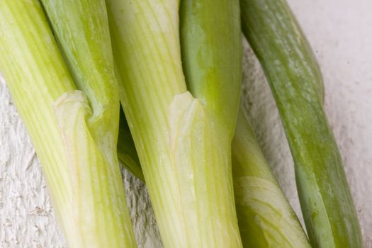 Overhead view of a bunch of fresh leafy leeks or scallions lying on white painted wooden boards