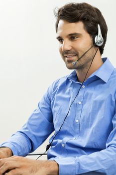 Attractive unshaven young man wearing a headset offering online chat and support on a client services of help desk as he types in information on his computer