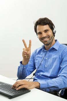 Attractive unshaven young man wearing a headset offering online chat and support on a client services of help desk as he types in information on his computer